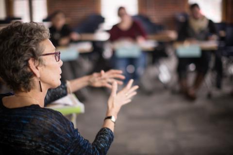 Professor addressing a class of students, she is lecturing animatedly with her hands